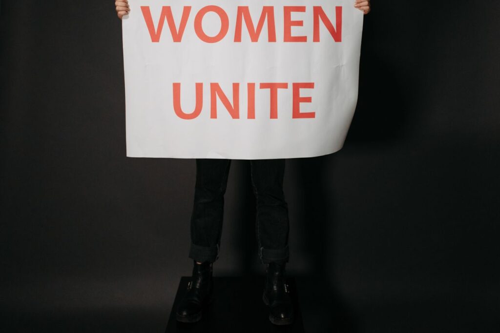 Studio shot of hands holding a 'Women Unite' poster against a black background, symbolizing empowerment.